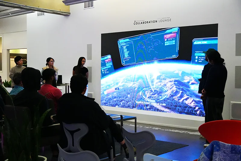 A presentation features people discussing in a room labeled "COLLABORATION LOUNGE," with a large digital screen displaying a map interface and text: "Monitor forest zones at scale."